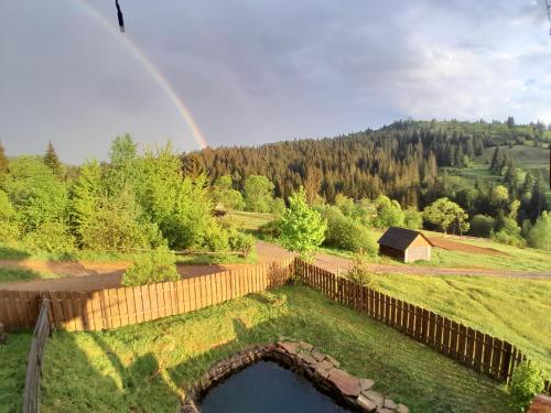 a rainbow over a yard with a pond and a fence at Villa Filiak in Yablunytsya