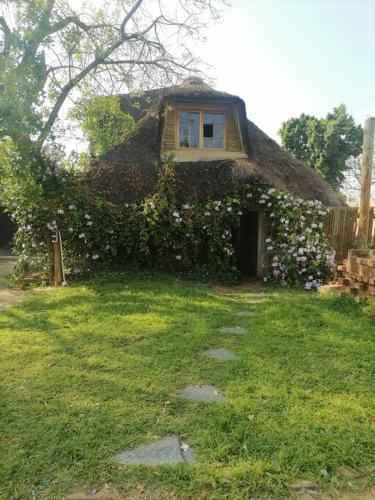a house with a thatch roof with flowers at Sweet Melody Tree House in Gaborone