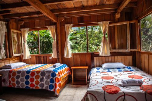 two beds in a room with windows at La Casa de Cecilia Mindo in Mindo