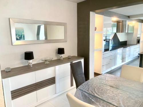 - une cuisine avec des placards blancs, une table et un miroir dans l'établissement grande villa piscine Marseillan plage cap agde, à Marseillan