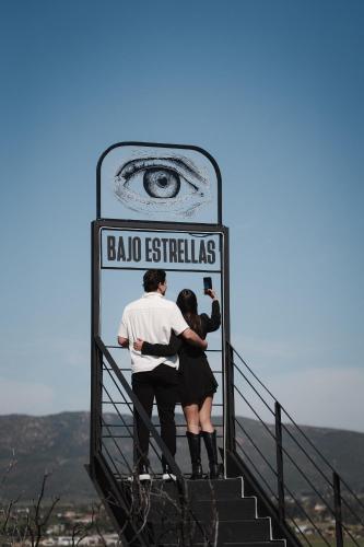 a man and a woman standing on the steps of a sign at Bajo Estrellas Hotel Contemporáneo in Valle de Guadalupe