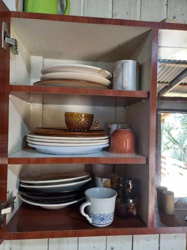 a shelf with plates and cups and dishes on it at Cabana de pesca e lazer Represa Usina Mafra sc in Mafra