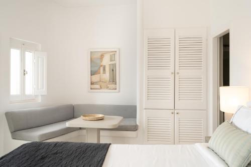 a white bedroom with a couch and a table at Aqua Luxury Suites by NOMÉE Hospitality Group in Imerovigli