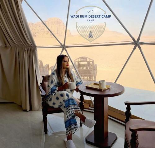 Wadi Rum desert camp في وادي رم: امرأة تجلس على طاولة مع كوب من القهوة