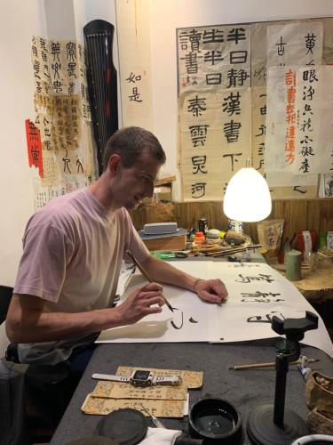 a man sitting at a table writing on a piece of paper at Zhangjiajie One Art Guesthouse in Zhangjiajie