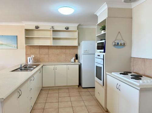 Una cocina con gabinetes blancos y un refrigerador blanco. en Pelican Shore Villa 14 - Kalbarri WA, en Kalbarri