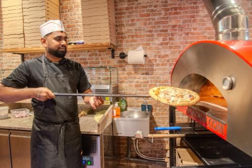 a man taking a pizza out of a pizza oven at Casa Serena Paris Hôtel in Paris
