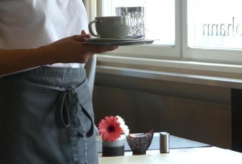 a person holding a plate with a cup and a flower at Das Reinisch Hotel - near Vienna Airport in Schwechat