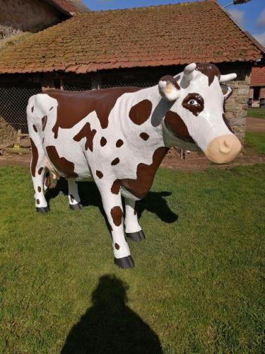 une statue d'une vache debout dans l'herbe dans l'établissement Camping à la ferme de la tournerie, à Raids