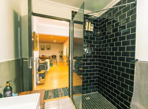a bathroom with a glass shower with a black tile wall at The Green Door Cottage in Roodepoort