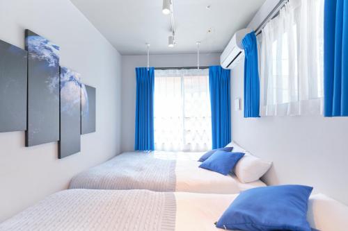 two beds in a bedroom with blue curtains at Blighton Miyoshi by Tranova in Tokyo