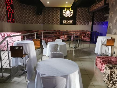 um restaurante com mesas e cadeiras brancas e um relógio em Ebony Lounge Hotel and Event Center em Pretoria