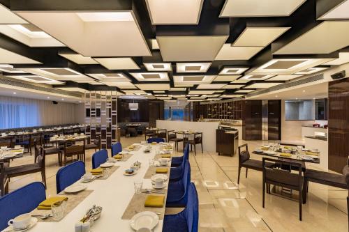 RPJ Hotel Rajkot في راجكوت: غرفة طعام مع طاولات طويلة وكراسي زرقاء