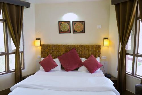 a bedroom with a white bed with red pillows at Whispering Winds Resort in Dharamshala
