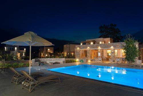 a swimming pool at night with two chairs and an umbrella at Vourkari Village in Vourkarion