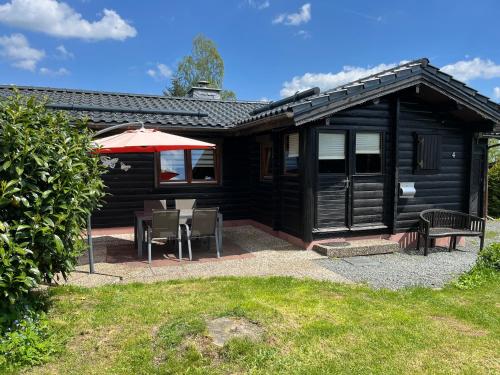 a black cabin with a table and an umbrella at Blockhaus FerienZauber in Bromskirchen