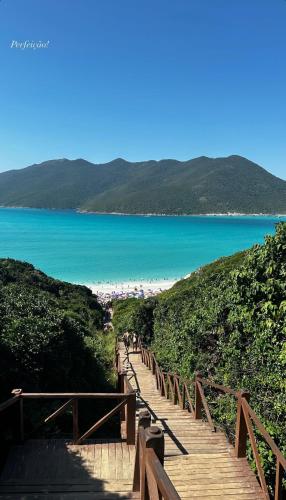 a wooden boardwalk leading to a beach with the ocean at Loft Santorini com hidro aquecida - Arraial do Cabo in Arraial do Cabo
