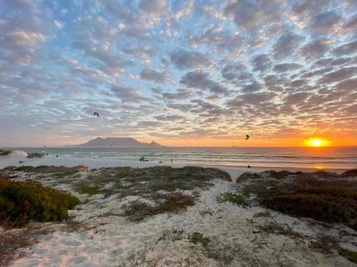 a sunset on a beach with people flying kites at Dolphin Beach Cabana in Table View