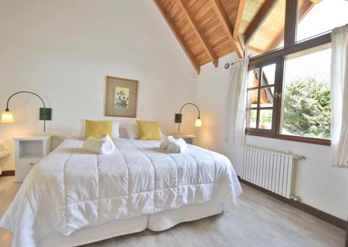 a bedroom with a large white bed with a large window at Plaza Mayor by Visionnaire in San Martín de los Andes