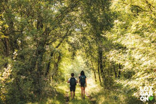 two people walking on a path through a forest at Gîte Mara des Bois - Domaine du Pi geonnier de Saint-Vincent in Bourran