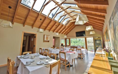 un comedor con mesas y sillas blancas y ventanas en Rosas Blancas Apart Hotel By Visionnaire en San Martín de los Andes