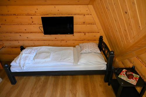 a bed in a wooden room with a tv on a wall at Zbojnicky penzion in Oravska Jasenica