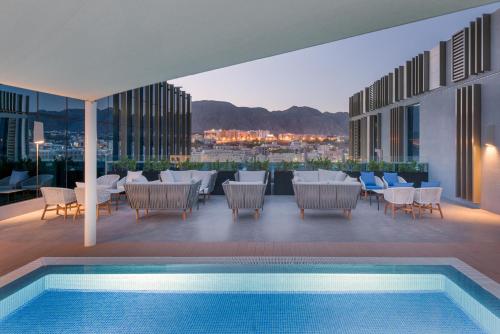 a pool on the roof of a building with tables and chairs at IntercityHotel Bawshar Muscat in Muscat