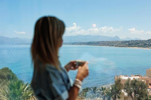 a woman taking a picture of the water at Marina di Petrolo Hotel & SPA in Castellammare del Golfo