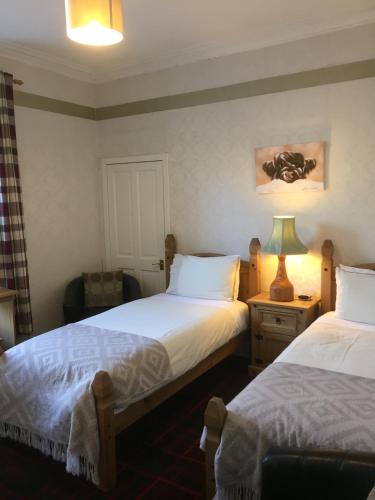 a bedroom with two beds and a lamp on a table at Tanglin Guest House in Oban