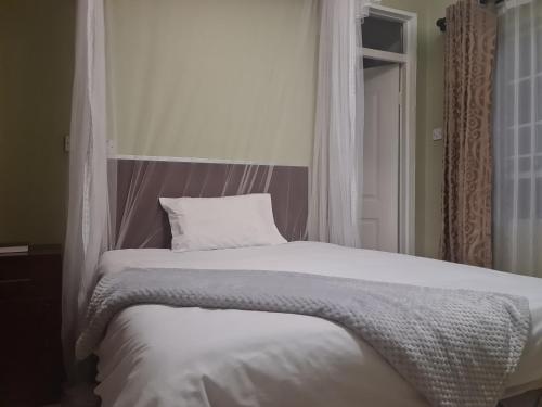 a bedroom with a bed with white sheets and a window at The Cottage in Lilongwe