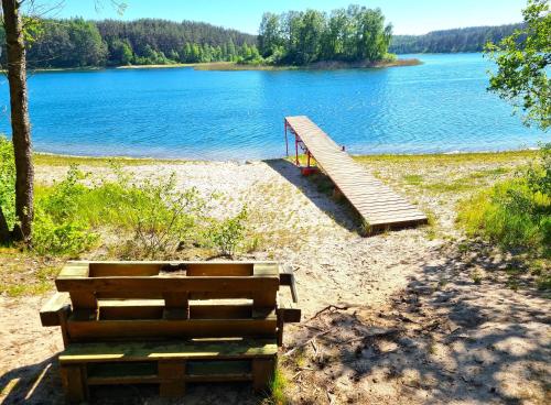a wooden bridge over a lake with a bench at Chatka Baby Jagi - Domek z balią i kominkiem w lesie pośród jezior in Niesiołowice