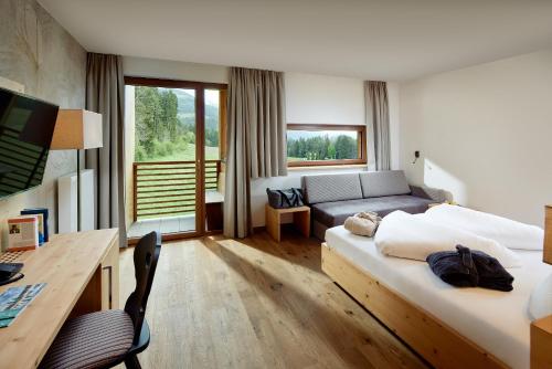 a bedroom with a bed and a desk and a couch at Naturhotel Die Waldruhe GmbH in Chienes