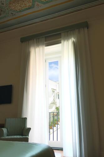 a bedroom with a window with white curtains and a chair at Aqua Mirabilis Relais de Charme in Minori