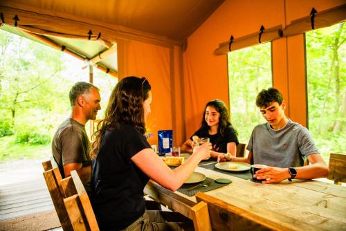 a group of people sitting around a wooden table at Luxury Safari Tent with Hot Tub in Ancient Woodland in Acton Scott