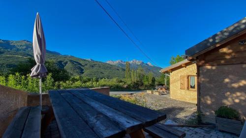 a wooden picnic table with an umbrella and a building at L'Intermède & En toute amitié - Les Gites de l'Argile in Faucon-de-Barcelonnette