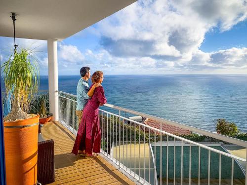 a man and woman standing on a balcony looking at the ocean at Indigo Star House in Ribeira Brava
