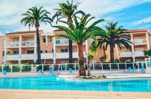 a swimming pool with palm trees in front of a building at Votre résidence de vacances avec piscine, tennis, à 2 minutes de la mer in Vallauris