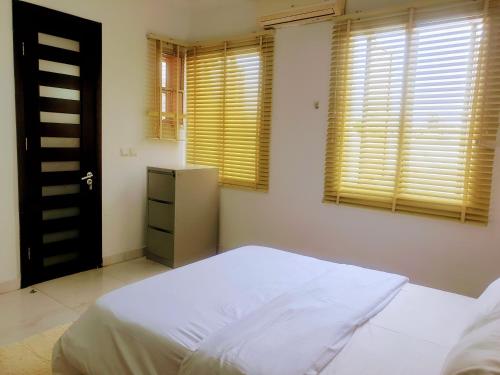 a bedroom with a white bed and two windows at Oasis in the City. Victoria Island serviced apt. in Lagos