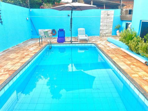 a blue swimming pool with an umbrella and chairs at CASA EM FOZ DO IGUAÇU DESTINO DO MUNDO in Foz do Iguaçu