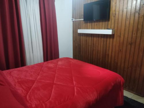 een slaapkamer met een rood bed en een tv aan de muur bij Hostal NFrocket in Los Ángeles