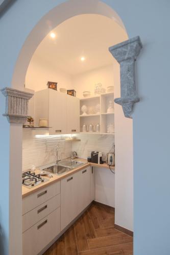 a kitchen with white cabinets and a sink and an archway at La Chicca Sicily Holiday House in Castelmola