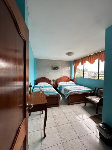 1 dormitorio con 2 camas, mesa y puerta en Kanoas Hostal, en Puyo