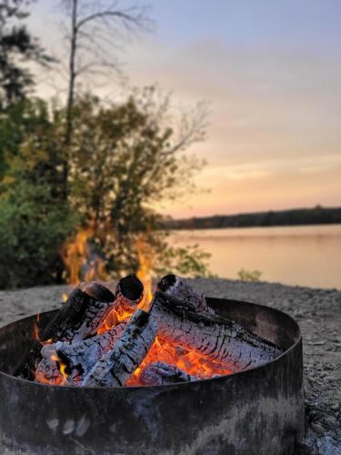 a fire pit on the beach next to a lake at Spot Caché - Private Waterfront Cottage in Papineauville