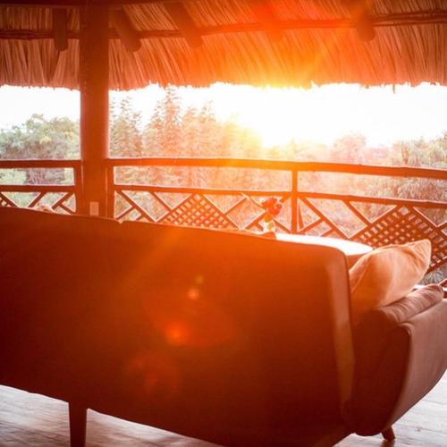 a couch on a porch with the sun shining through a window at Hotel Restaurante Mi Jardin Troncones in Troncones