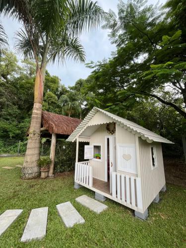 a small white play house in a yard with a palm tree at Familien Haus Pousada in Pomerode