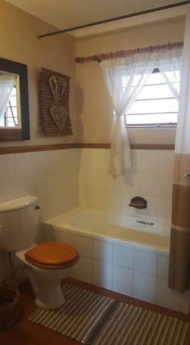 a bathroom with a toilet and a tub with a window at UrbanEscape in Centurion