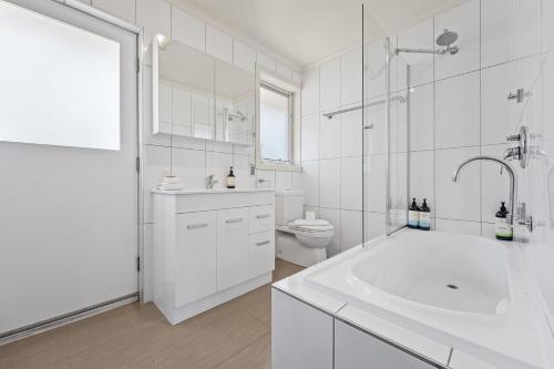 a white bathroom with a tub and a toilet at Sponars Onshore - 2BR Apartment l Pet-Friendly l WiFi l Air-Con l Fenced Backyard in Jindabyne