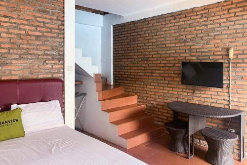 Cette chambre est dotée d'un mur en briques, d'un lit et d'une télévision. dans l'établissement Urbanview Hotel Villa Q Gisting, à Banjarnegeri