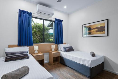 two beds in a room with blue curtains at Cable Beachside Apartments in Broome