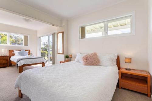 a white bedroom with two beds and two windows at Your home at Cockle Bay in Auckland